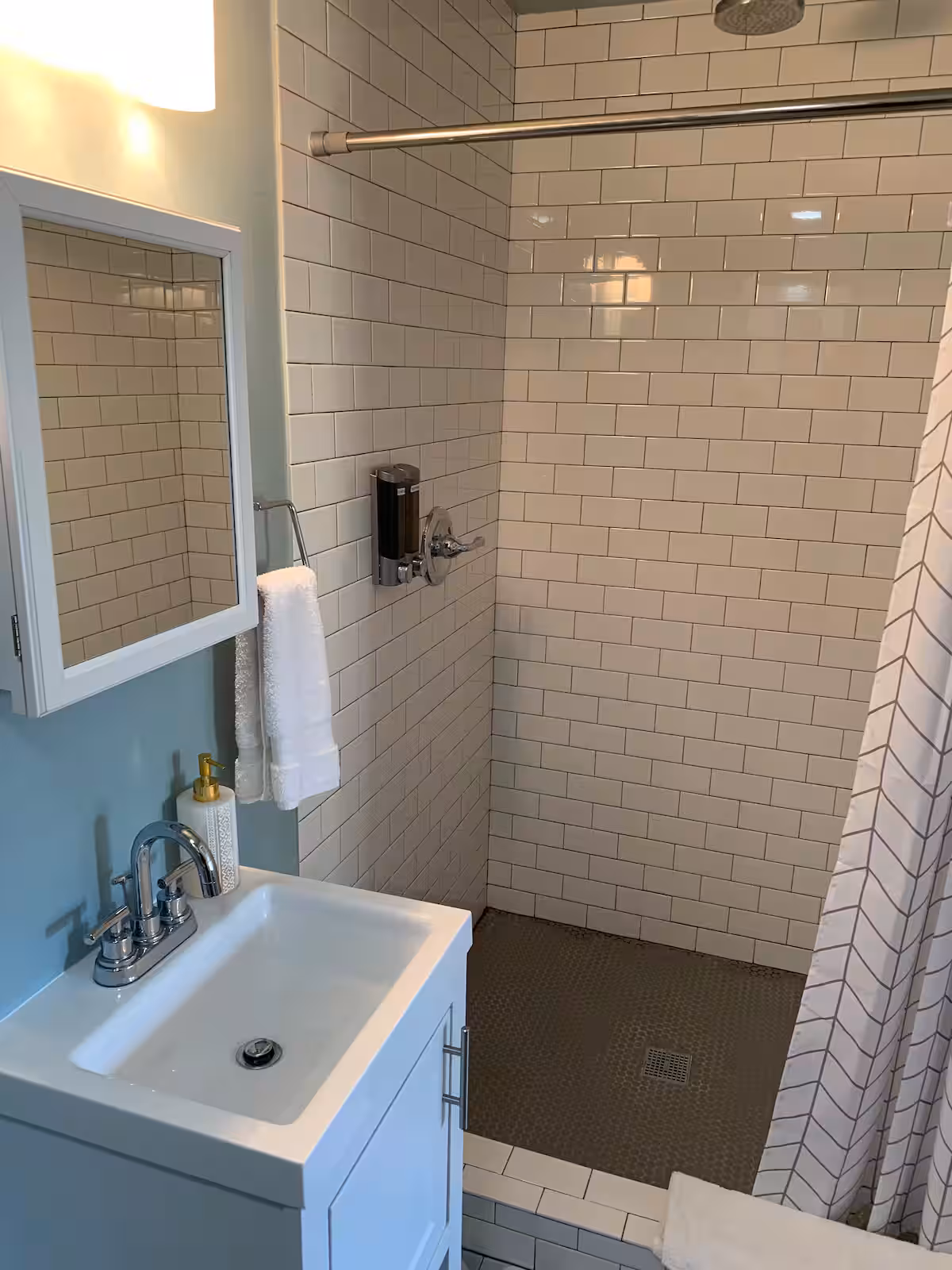 White subway tile walk-in shower with herringbone curtain and geometric floor tile