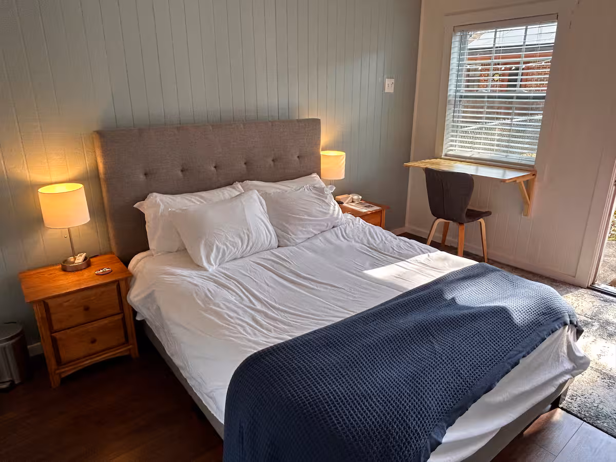Bright bedroom with sage green walls, queen bed with white linens, warm bedside lamps, natural light streaming in