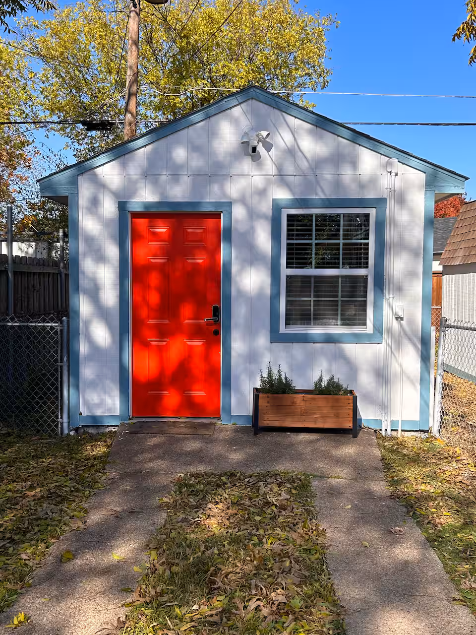 Casita on the Park — charming white guesthouse with a bold red door, sage green trim, surrounded by greenery